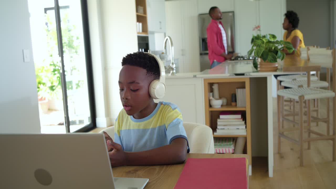 African American family with child taking online lesson at kitchen table with laptop headset pencil
