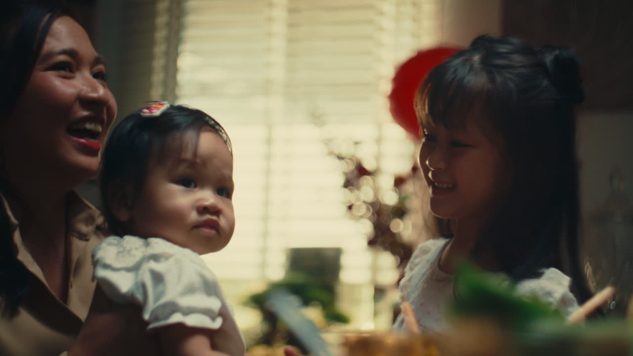 Loving mother holds baby while big sister smiles in a warm family moment indoors