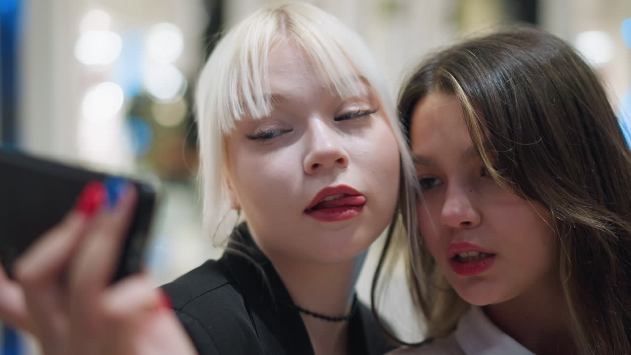 Two cheerful girls making video indoors on smartphone with joyful and excited expressions as they smile and react playfully creating fun social moment filled with energy friendship