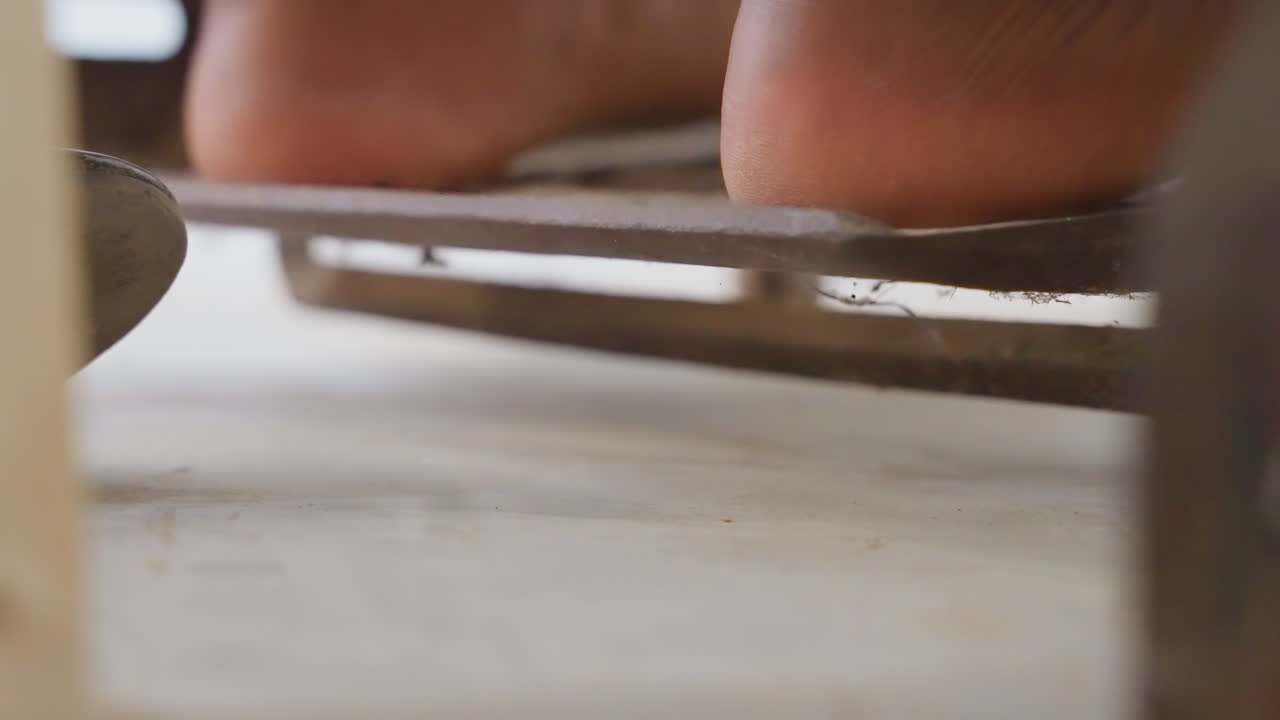 Close up bare toes on metal pedal driving antique treadle in home workshop barefoot artisan pressing pedal to mend fabric and linen, slow rhythmic motion across worn plate, close texture of skin