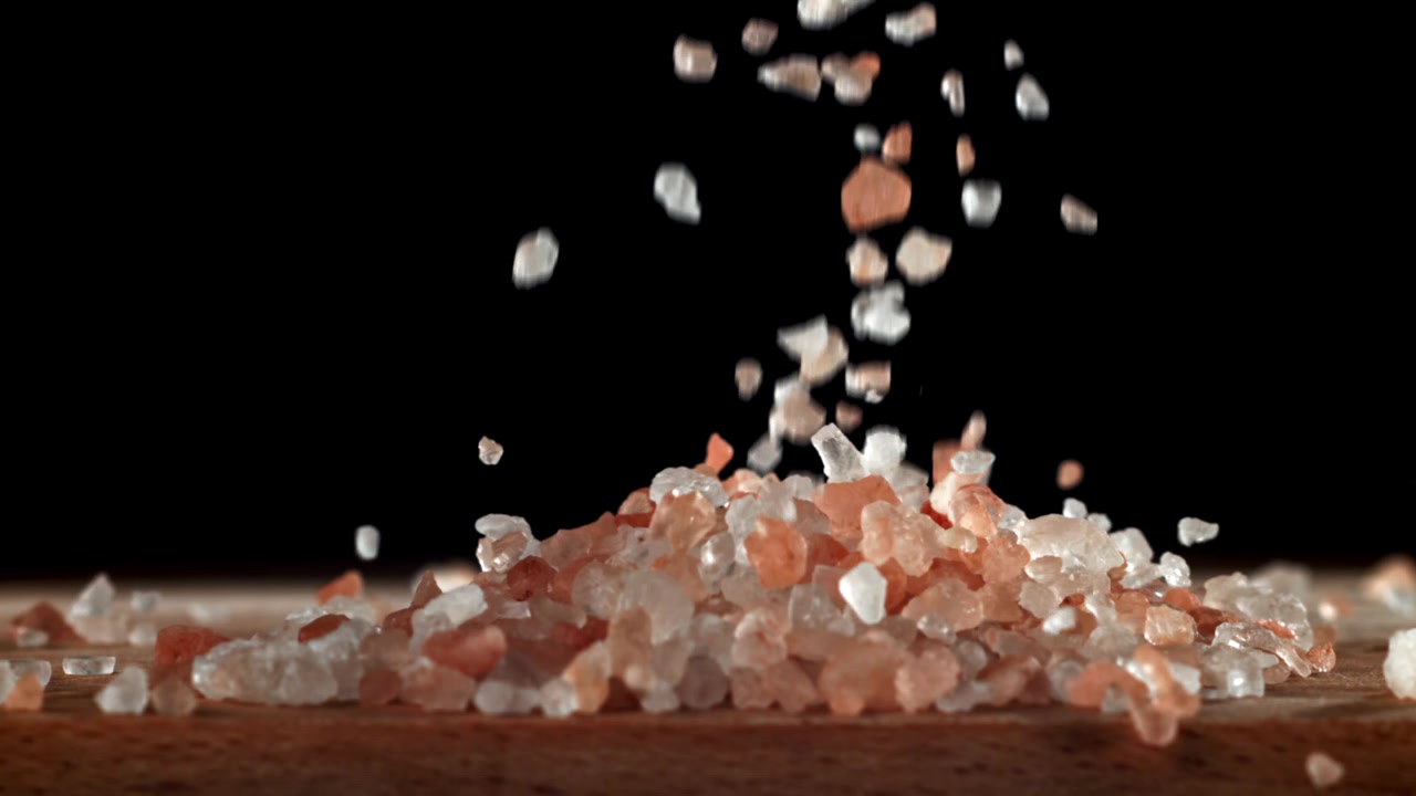 Slow motion af lyserødt Himalayasalt, der falder på en træoverflade