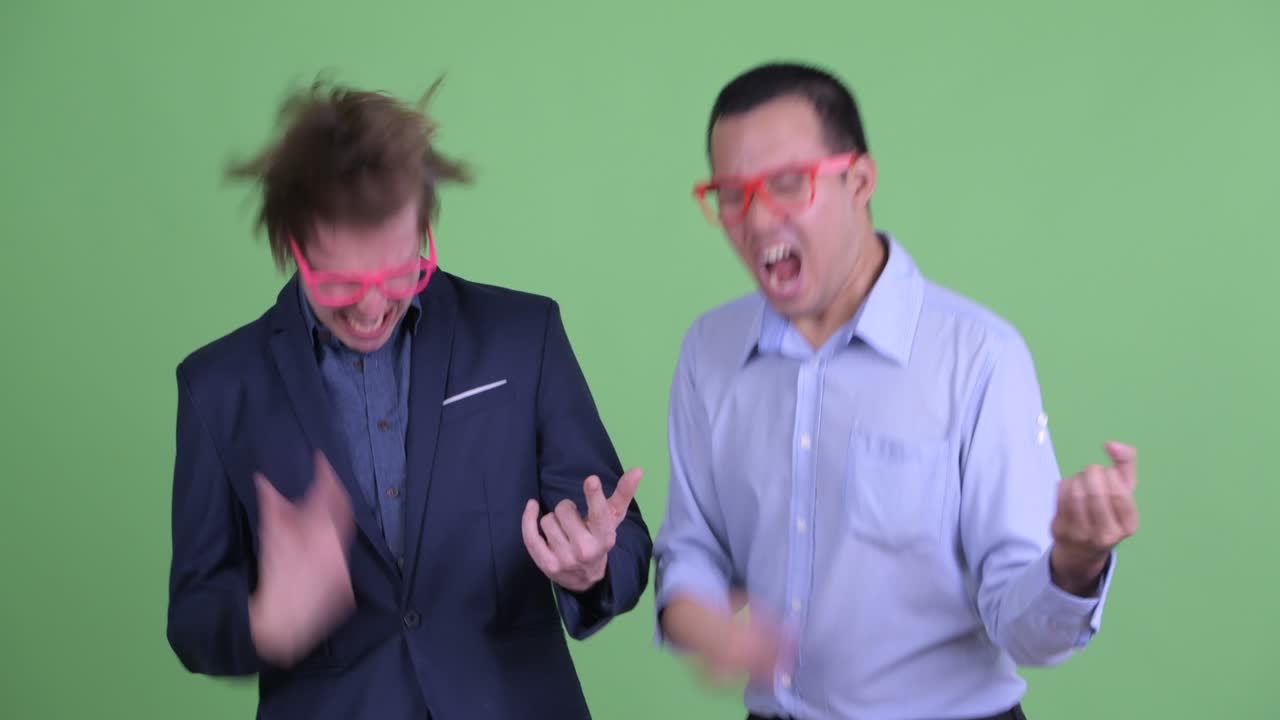 두 명의 괴짜 사업가가 녹색 스튜디오 배경에 공기 기타를 춤추고 연주하고 있습니다.