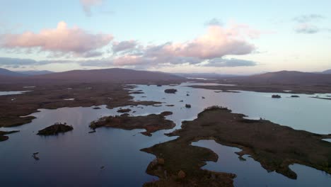 a drone slowly rises above a patchwork landscape of islands amongst fresh water lochs and peat bogs at sunset