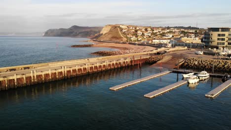 Downwards-pedestal-aerial-shot-looking-towards-the-cliffs-and-the-harbour-of-West-Bay-Dorset-England-UK