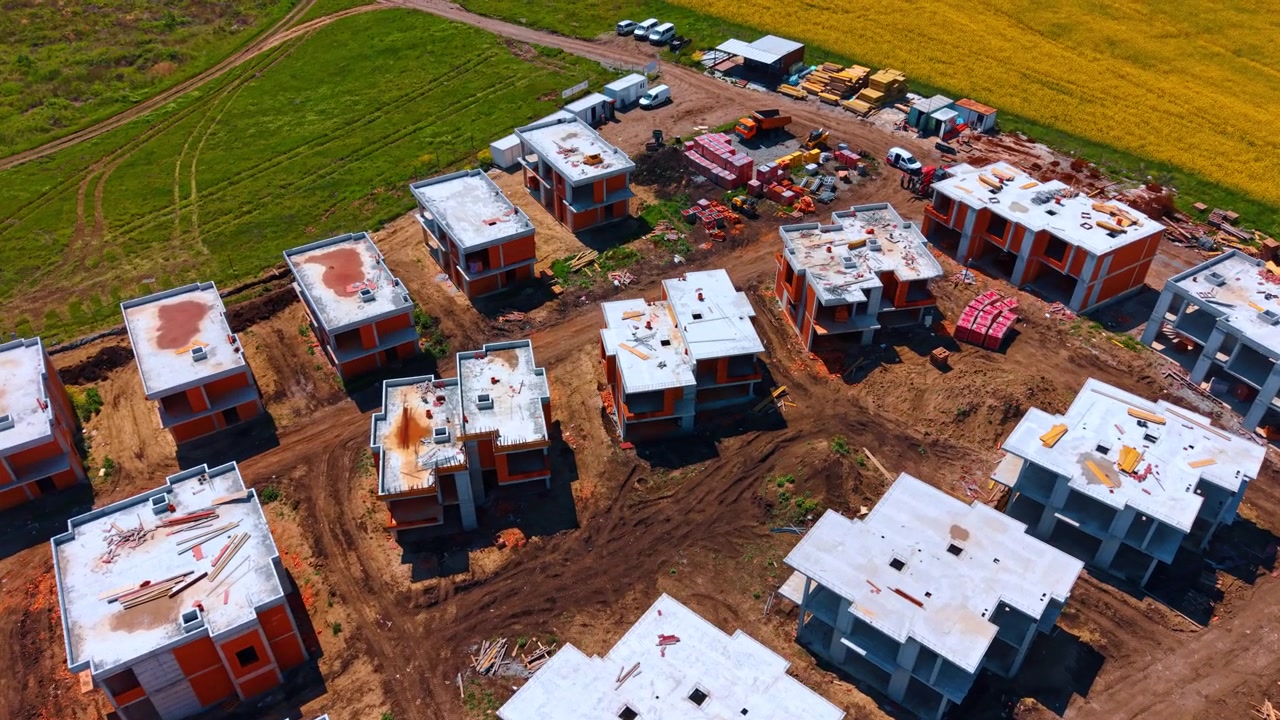 Vista aerea dall'alto di un cantiere per un villaggio residenziale di villette. Vista con drone dall'alto di più case in cemento e mattoni in fase di costruzione.