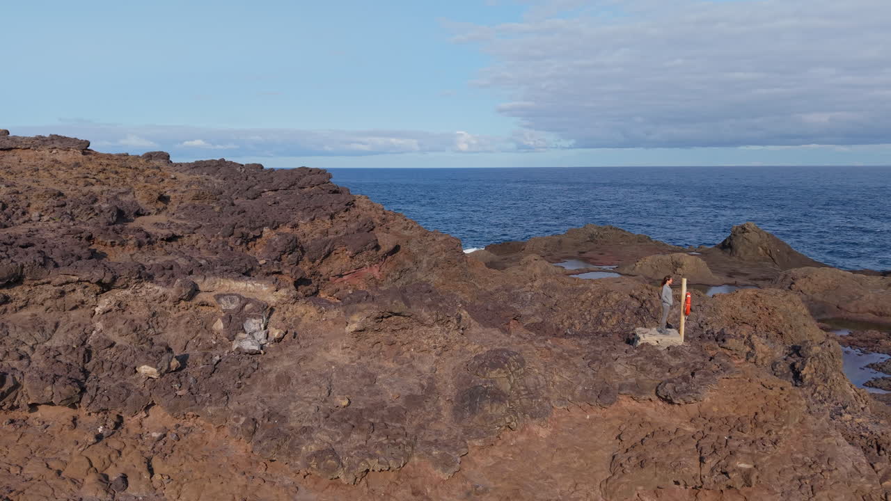 Mujer sobre rocas volcánicas cerca del faro de Punta Sardina, Gran Canaria, Islas Canarias, España.