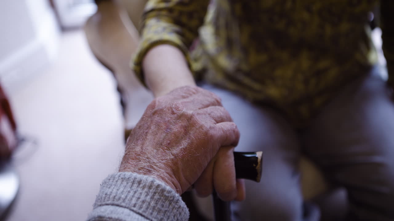 An elderly person's hand rests on a cane with support