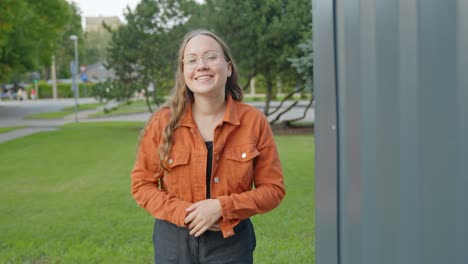 woman in casual attire smiles and holds her jacket in a green park