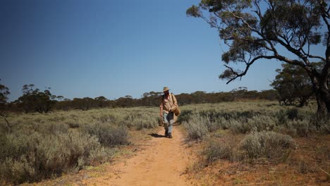 an old vintage looking swag man walks through the australian outback