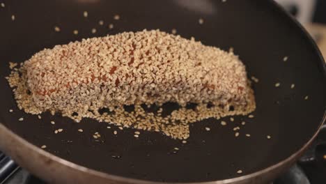 slowly swirl the oil around to coat the bottom of the frying pan with delicious seafood gourmet, salmon fillet covered with white sesame seeds cooking on the skillet, close up shot