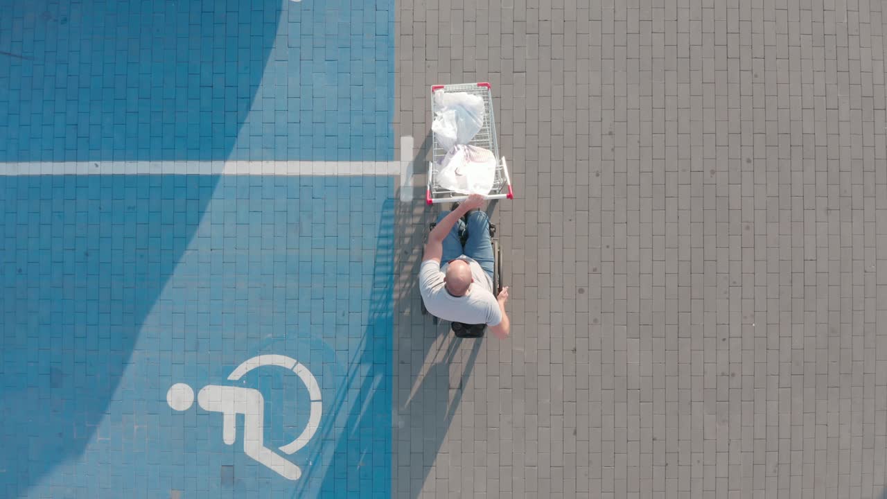 Man with disabilities in wheelchair pushing cart in front of himself at supermarket parking
