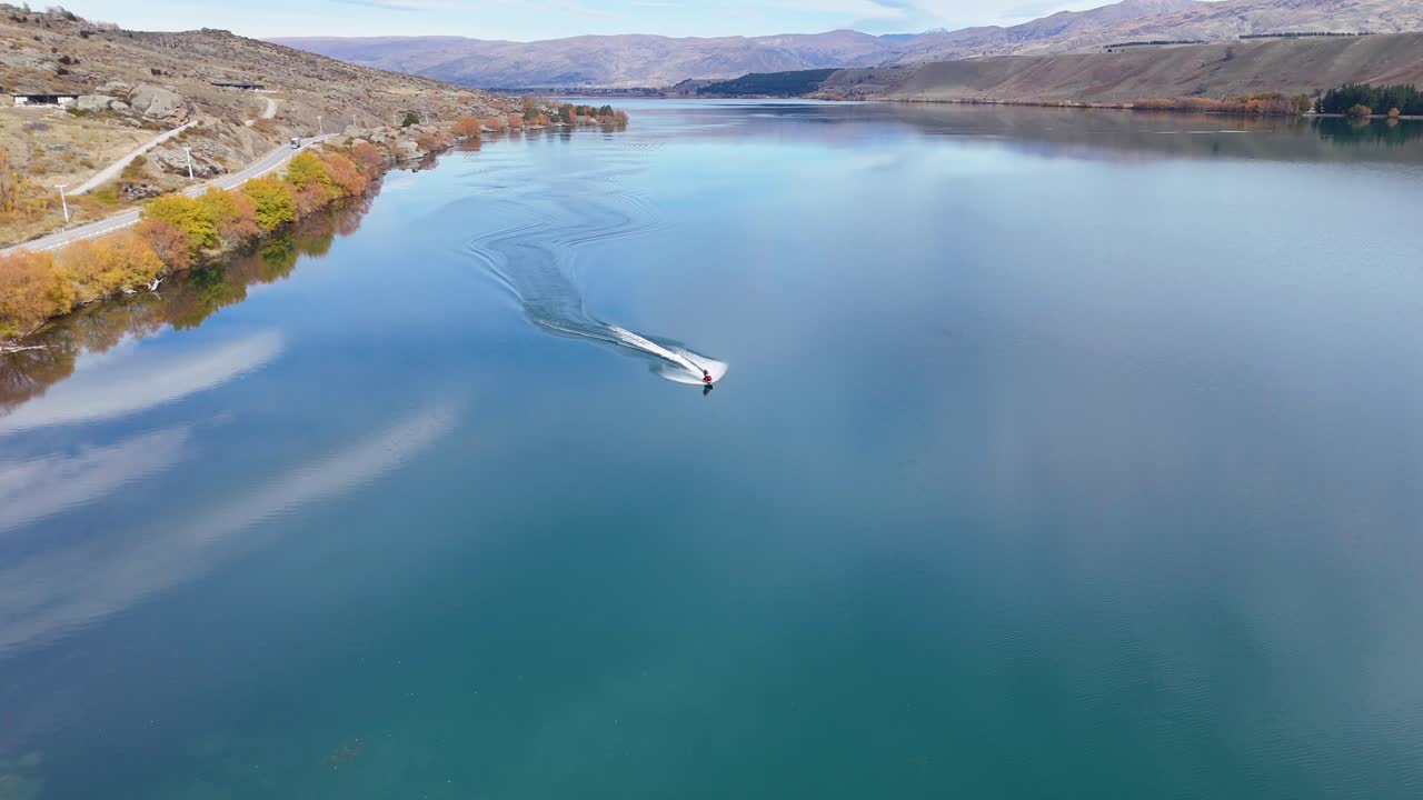 Aerial view of a jet ski navigating Lake Dunstan, surrounded by autumn foliage and mountains, under clear skies