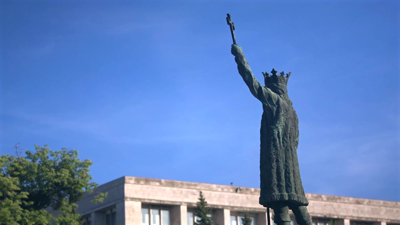 Statua di Stefano il Grande contro un cielo blu vivido, con alberi e architettura urbana sullo sfondo, Chișinău, Moldavia.