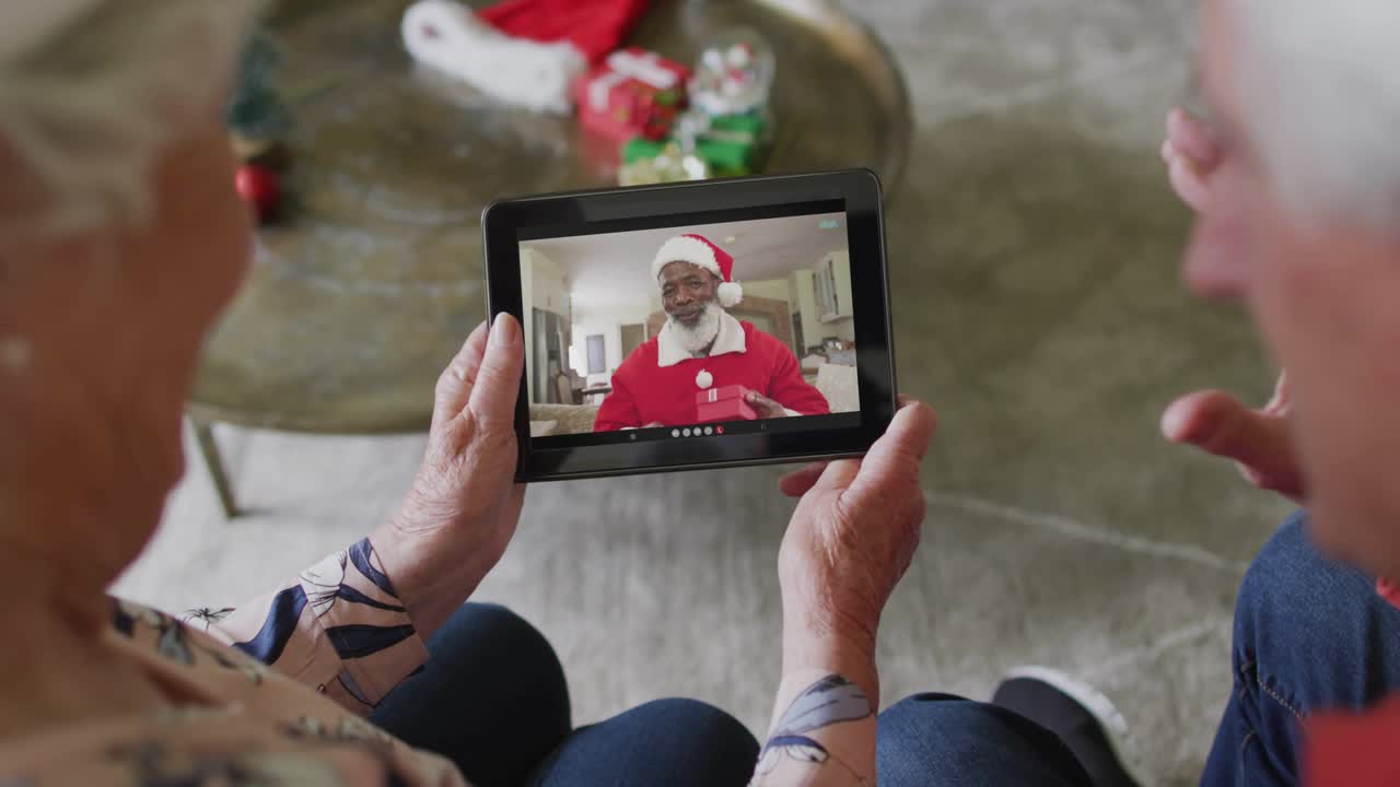 Coppia che tiene un tablet mentre riceve una chiamata per Natale e guarda Babbo Natale che mostra un bastone e un regalo, circondata da ologrammi