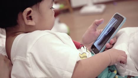 asian baby using mobile phones with mom on the bed