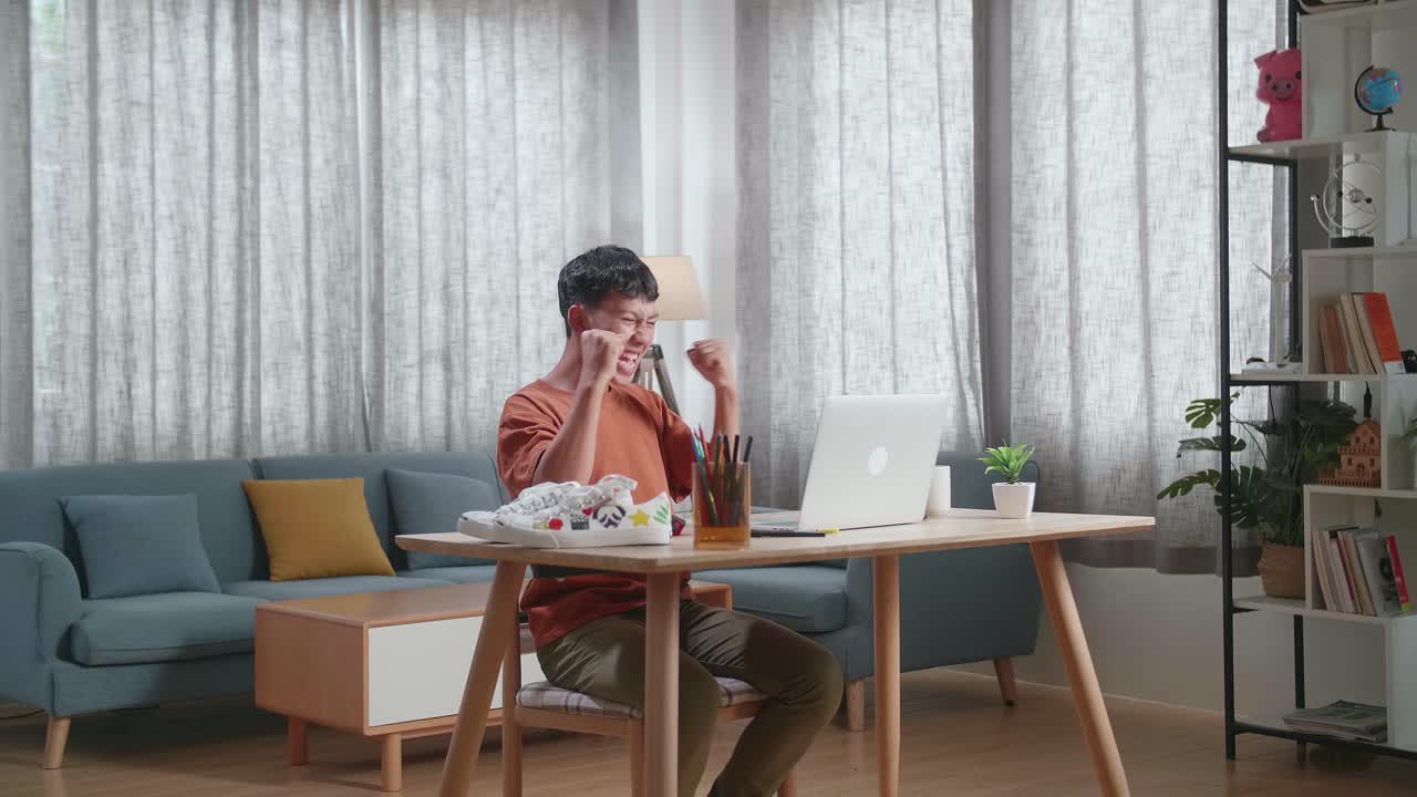 행복한 아시아 소년 신발 디자이너가 집에서 노트북으로 일하면서 축하하고 있습니다.