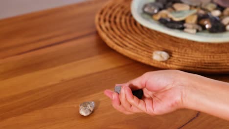 a hand tosses small rocks onto a wooden table, set against a warm, natural backdrop with soft lighting