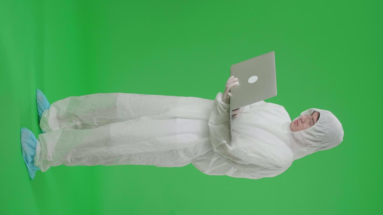 Side View Of Full Body Asian Man Wearing Personal Protective Equipment Uniform Ppe Holding And Working With Laptop Computer In The Green Screen Studio