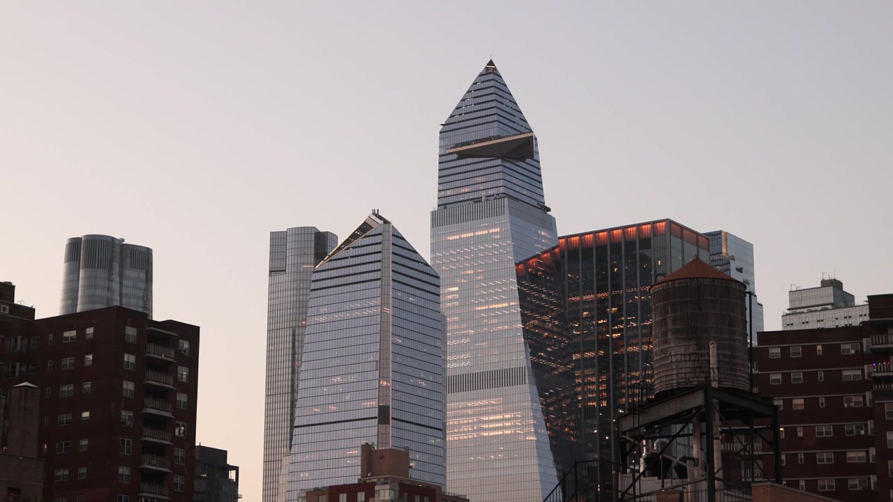 Tomada cinematográfica em ângulo baixo olhando para os imponentes arranha-céus modernos e a arquitetura icônica do horizonte de Nova York, silhuetados contra um dramático céu de pôr do sol em Manhattan