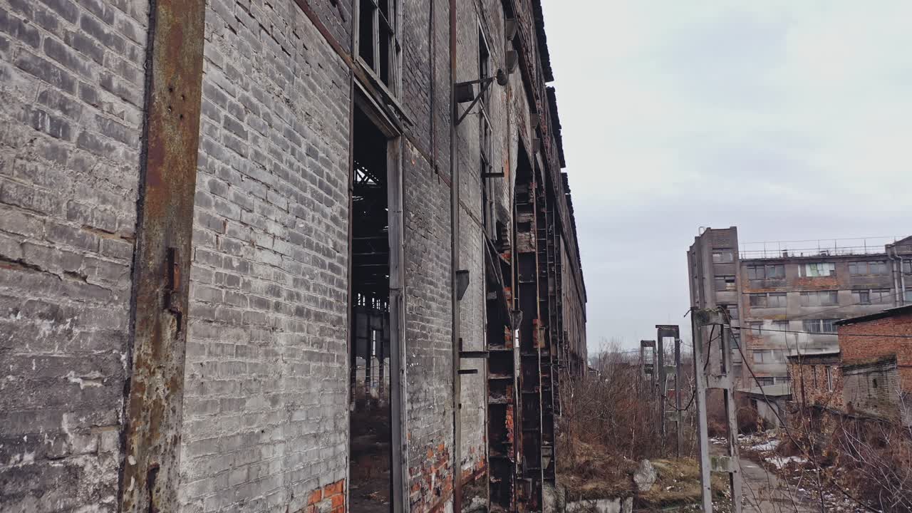 Former plant building with damaged brick walls and metal structures covered with moss on the roof and overgrowths inside and outside. Aerial view.