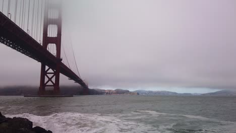 gimbal booming down shot of the rocky shoreline at fort point under the golden gate bridge on a foggy day in san francisco, california
