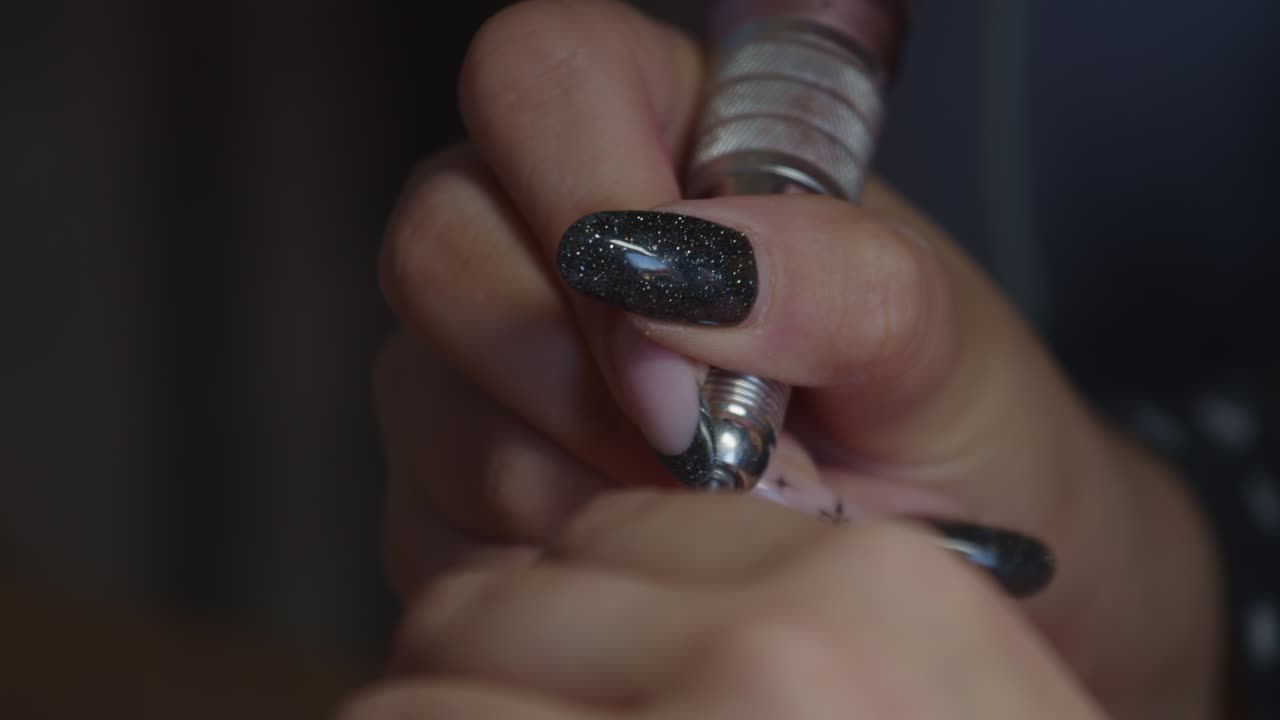Close up, manicurist using a nail drill to file, shape, and buff client's nails