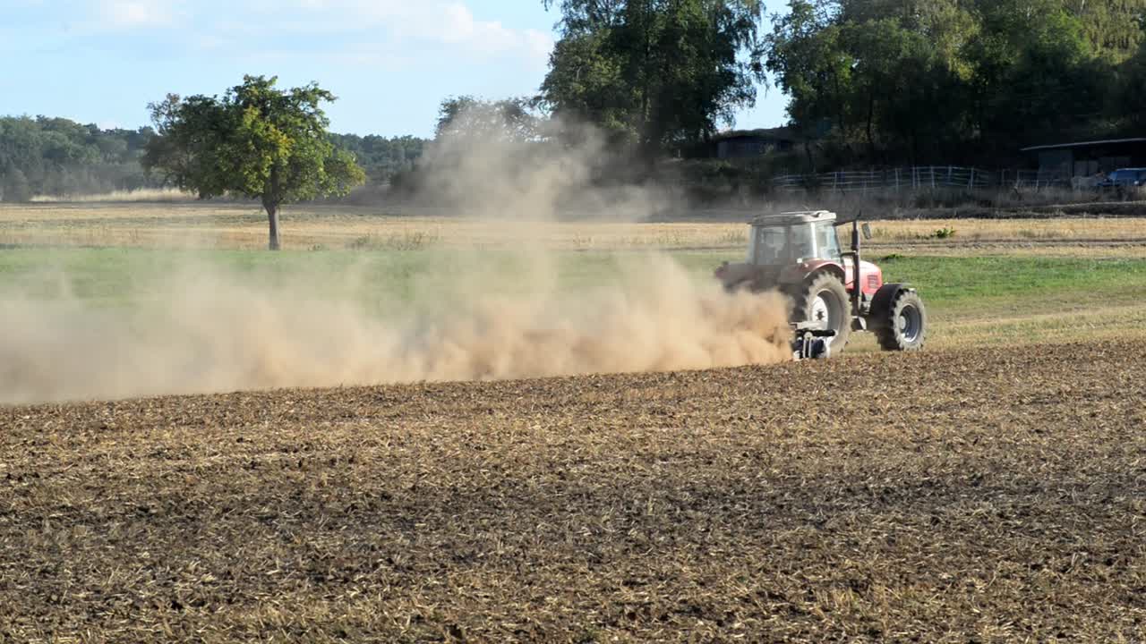 저녁 햇빛에 극도로 건조한 들판을 갈고 있는 작은 빨간 트랙터