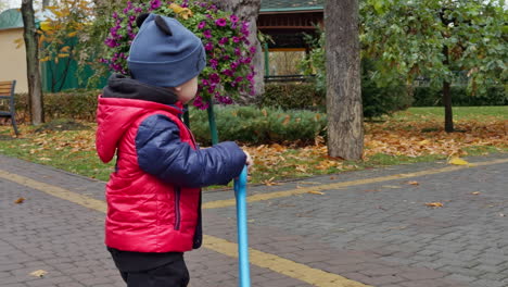 caucasian male kid with a toy in hands. toddler wearing warm clothes having a walk in the park in autumn.
