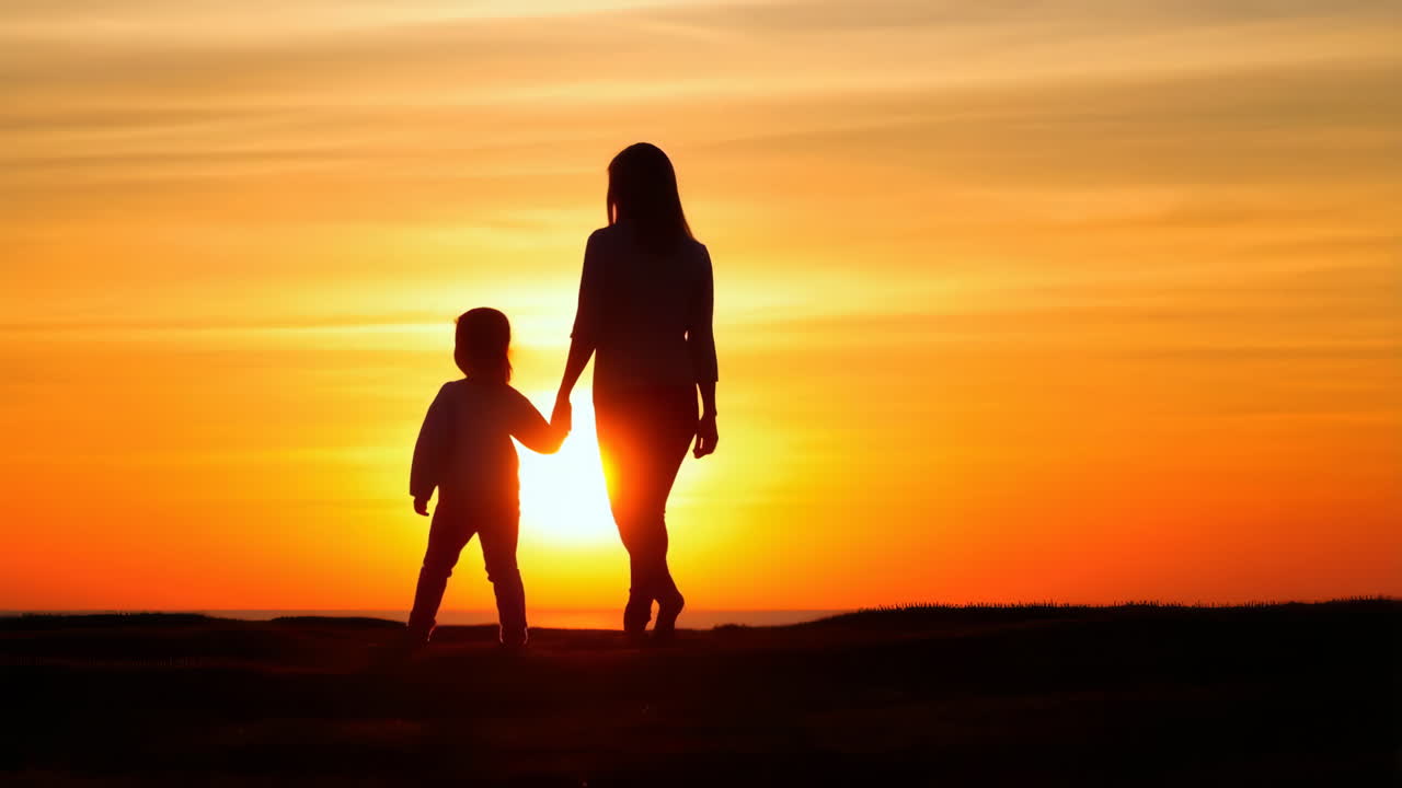 Mother and Child Silhouettes Walking Hand in Hand at Sunset