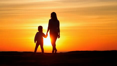 mother and child silhouettes walking hand in hand at sunset