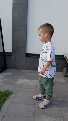 adorable baby boy running in the yard with green lawn. cheerful happy kid having active pastime outdoors. vertical video.