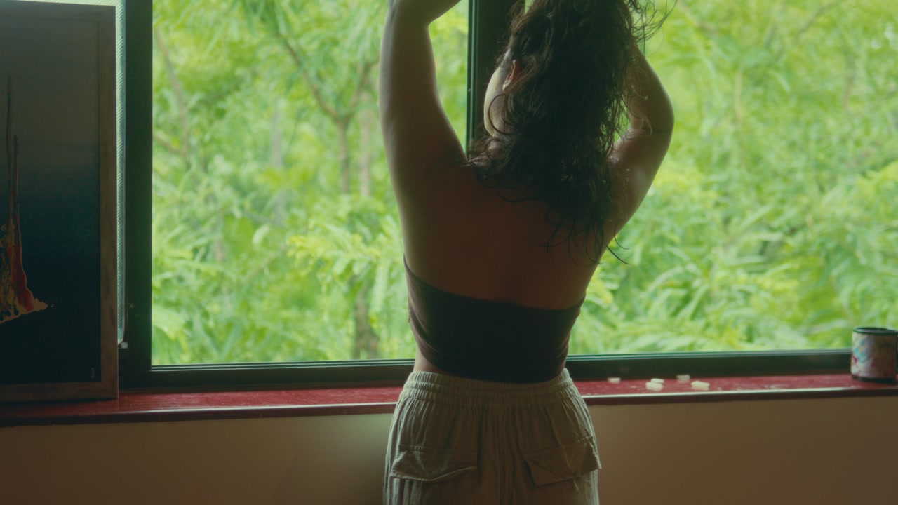 Back view of woman standing near window with soft natural light and green background calm indoor lifestyle moment