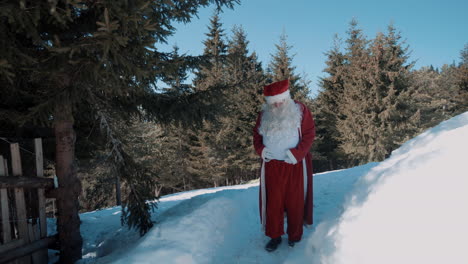 santa is walking on a snowy path along a wooden fence