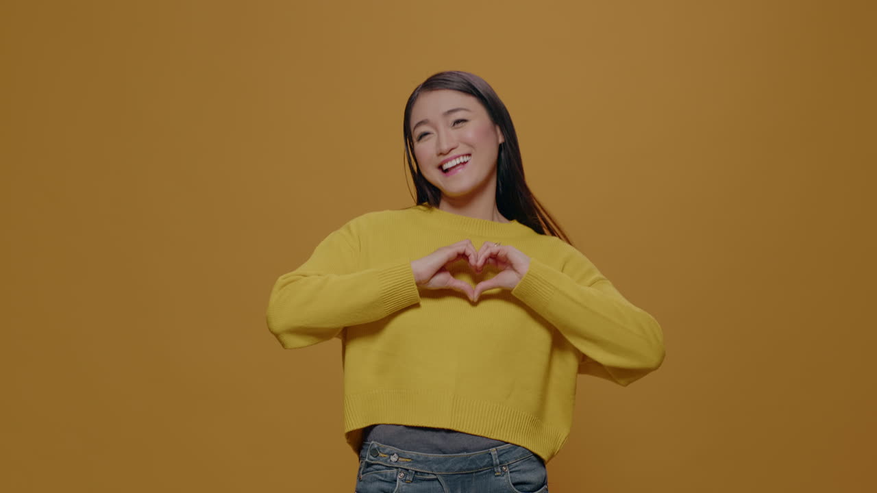 Portrait of woman showing heart shape gesture in studio