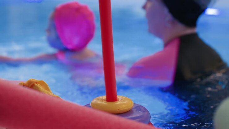 little child places ring toy into pool noodle, small hands focus on fit, water surface gleams, playful learning scene near pool edge, fine motor practice, joyful swim lesson captured