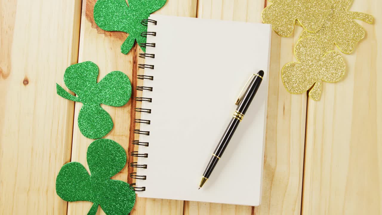 Video of st patrick's green shamrock and notebook with copy space on wooden background