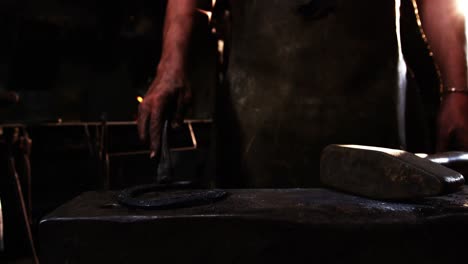 Mid-section-of-blacksmith-holding-horseshoe