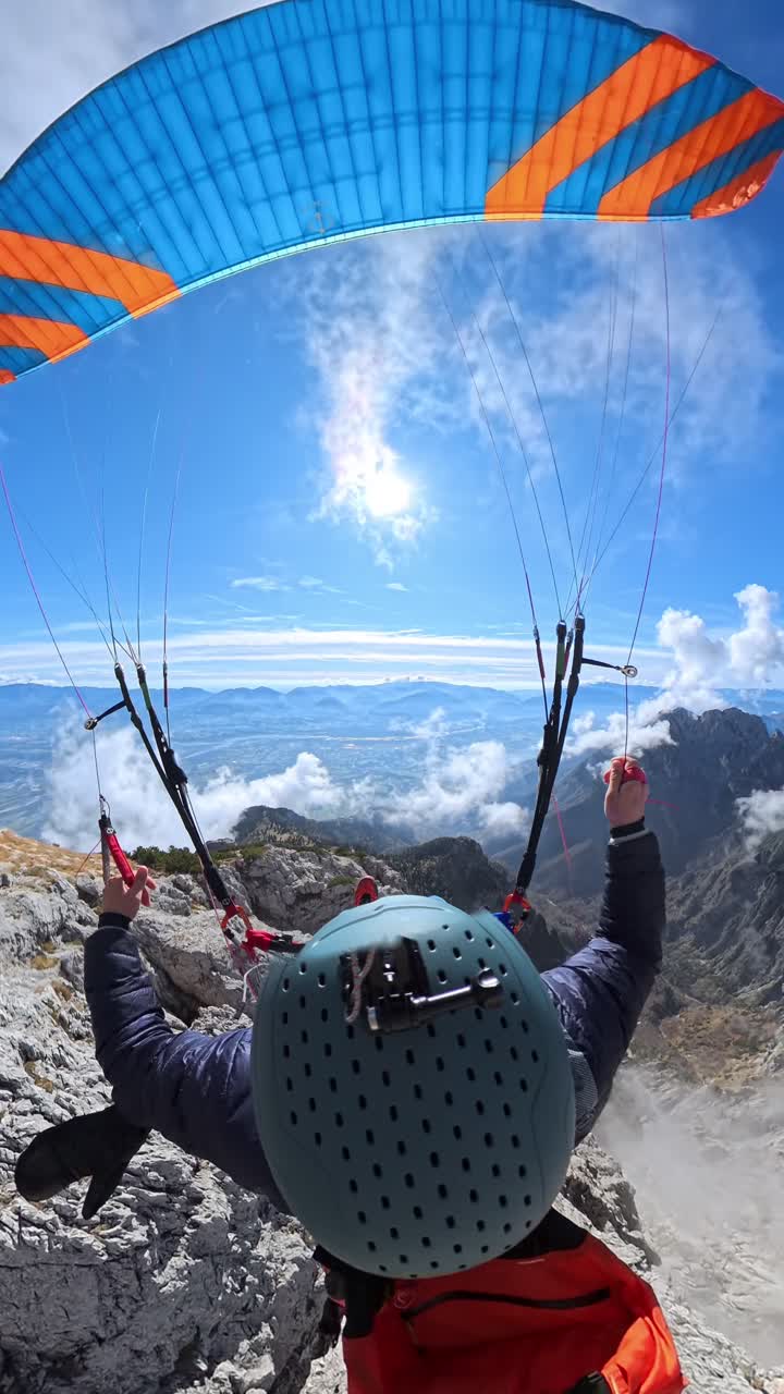 Seorang paralayang bersiap untuk lepas landas di lereng gunung berumput di bawah langit biru cerah - Bidikan Vertikal.