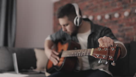 joven músico tocando y ajustando la guitarra en casa