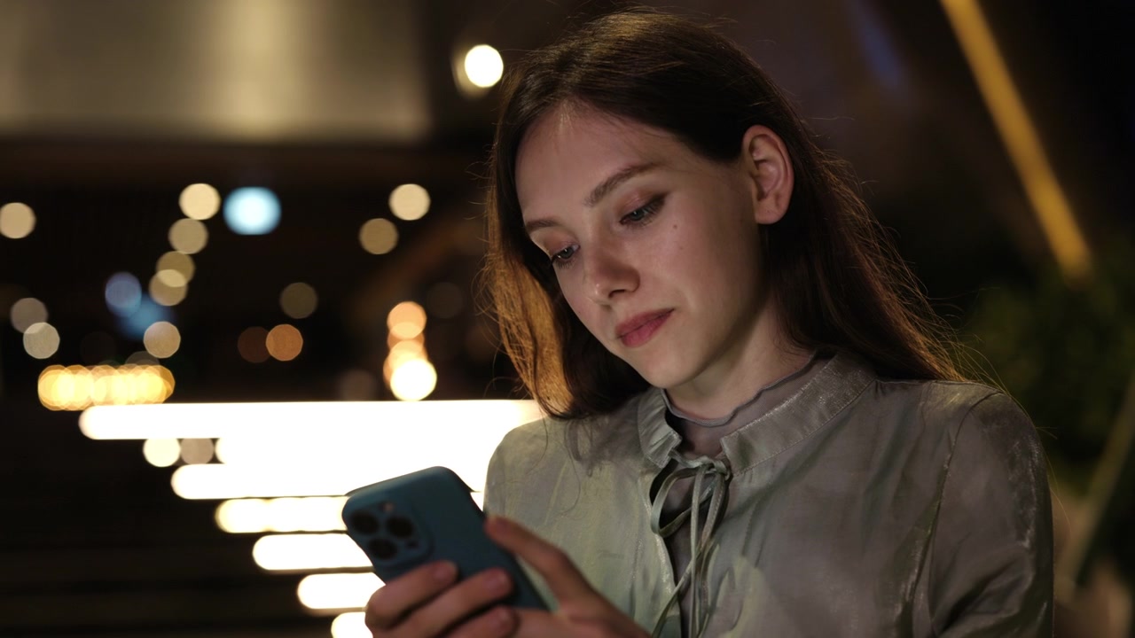 Giovane donna che usa lo smartphone di notte con luci bokeh