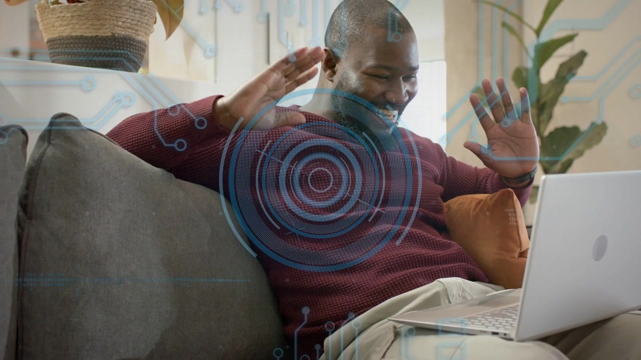 Mid adult man reacting to UI overlay, leaning into laptop, laughing and waving during remote work