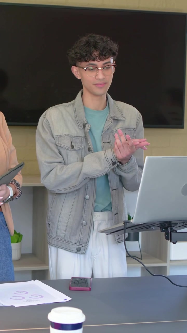 Vertical video: Colleague pointing tablet presenter jacket moving to laptop editing deck at meeting