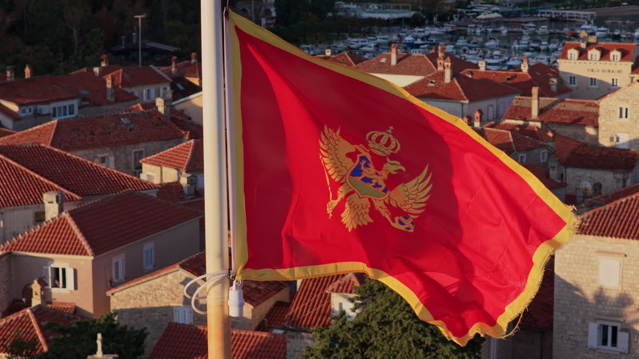 Aerial drone view of the Montenegro flag waving with Budva's Old Town and the marina in the background