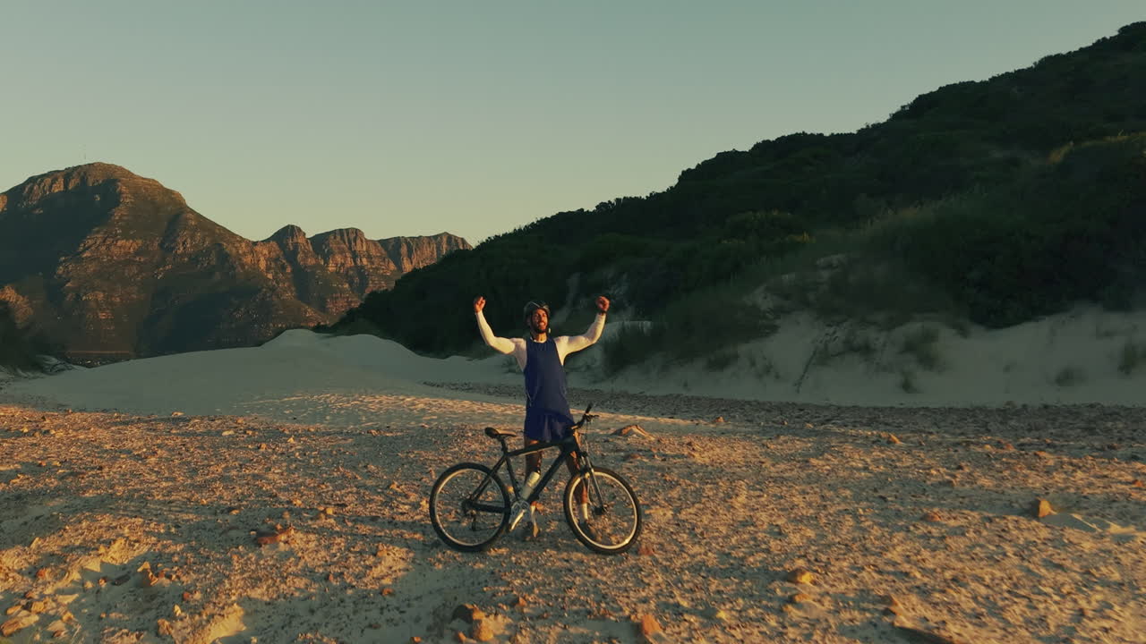 Homem com Bicicleta Comemora em Duna Arenosa ao Pôr do Sol
