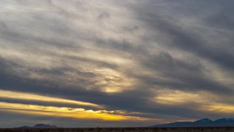 a golden sunset appears over the mojave desert landscape on an overcast day - wide angle time lapse