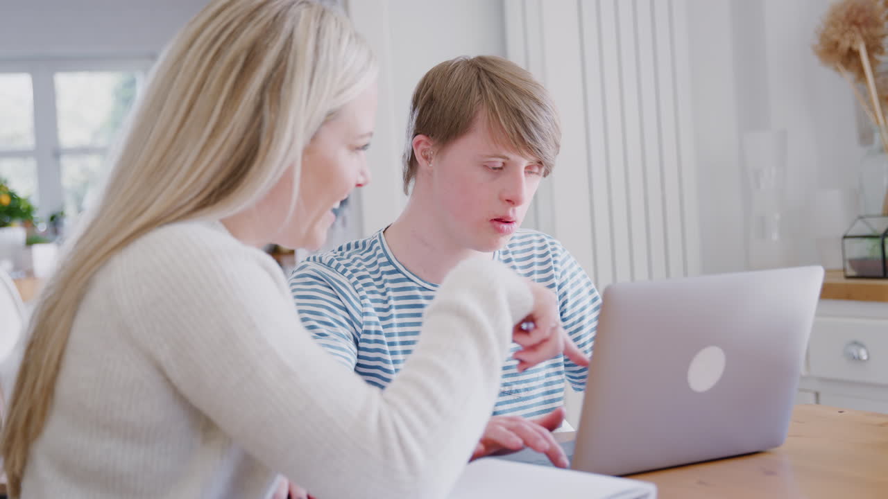 hombre con síndrome de down sentado con una maestra en casa usando una computadora portátil para la lección en casa