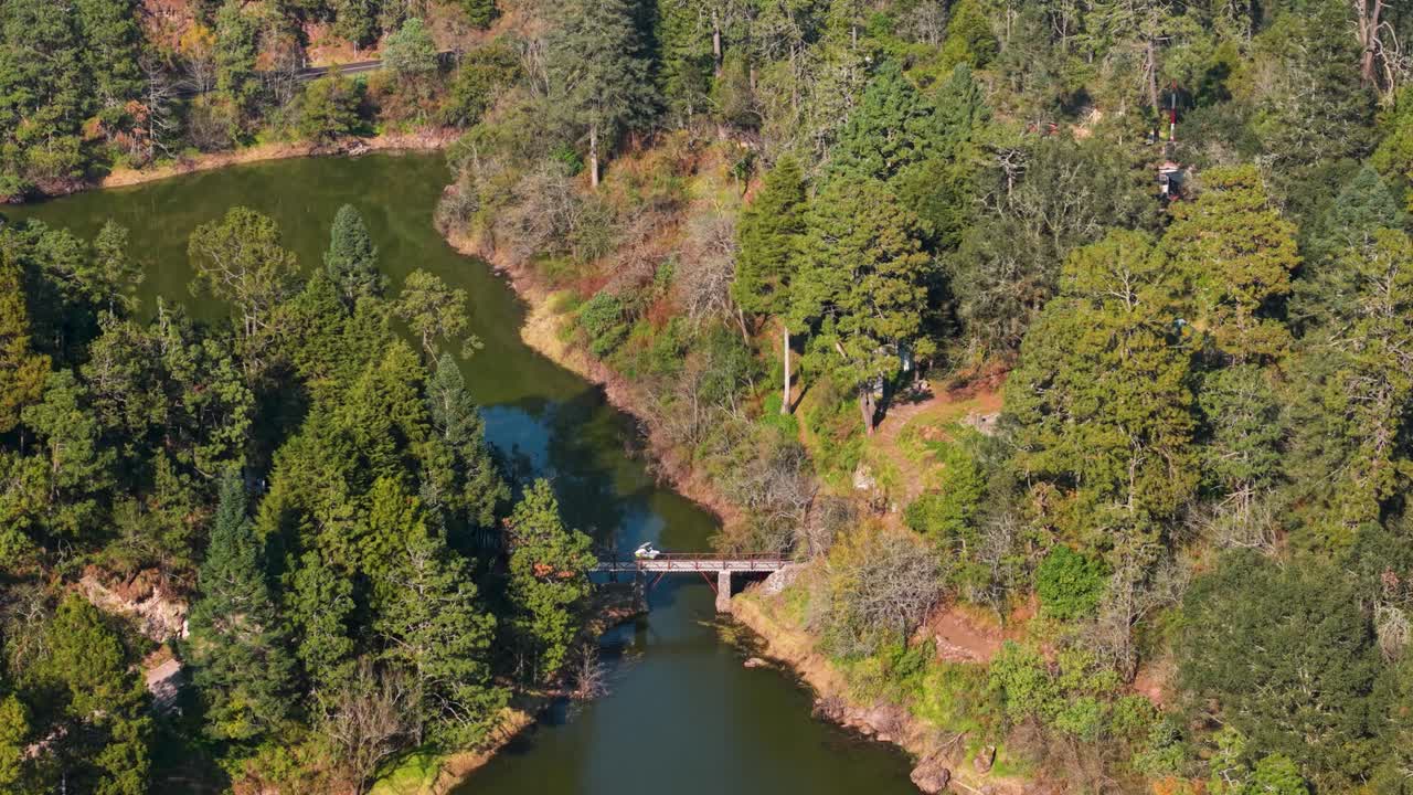 Drone shot of a bridge spanning mountains above a lake in a forested region