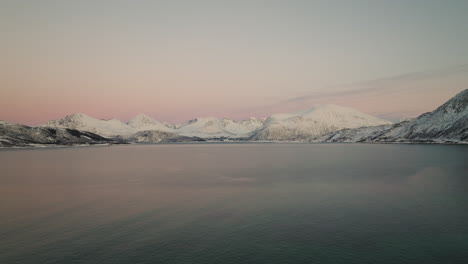 Puesta-De-Sol-Rosa-Sobre-El-Fiordo-Con-Montañas-Nevadas-En-El-Fondo,-Kvaloya,-Noruega---Toma-Aérea-De-Drones