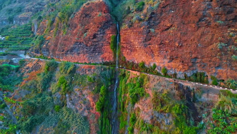 jaw-dropping view of a high mountain with a road in the middle. thin waterfall flows by the red rocks. aerial perspective on the nature of the madeira islands, portugal. drone footage.