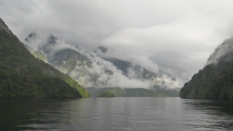 Slow-Motion-pan-across-mist-covered,-sun-dappled-mountains-in-Doubtful-Sound---Patea,-New-Zealand